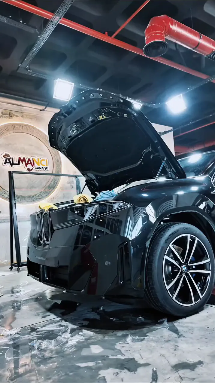 Almancı Garage atölyesinde kaputu açık siyah BMW iX; arkada yuvarlak Almancı Garage logosu